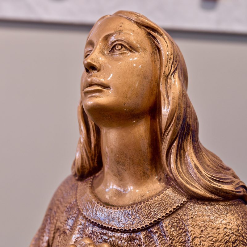 Statua scolpita a mano in bronzo raffigurante la Madonna che guarda verso il cielo. esempio di Arte Funeraria personalizzata inn bronzo.